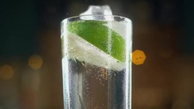 Katıksız soğuk buz küpleri, kireç dilimleriyüzen köpüklü suyun ıslak bardağına düşüyor. İçkide bir sürü baloncuk ve sıçrama var. Damlalar bir fincan aşağı akar