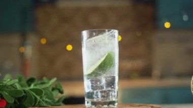 Taze sulu kireç dilimleri soda ve soğuk buz kristalleri ile cam kupa içine düşmek. Su etrafa sıçradı. Damlalar bardağa damlar. Etrafta Noel süsleri var. Panorama çekimi