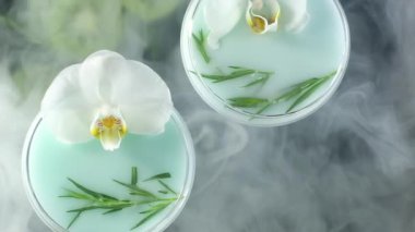 mavi bir kokteyl ile cam bardak, beyaz bir Orkide çiçek ve siyah bir taş standı üzerinde tarhun standı bir sprig. şenlikli içecekler dumanla örtülür. Üst te. Studio aydınlatma ile çekim