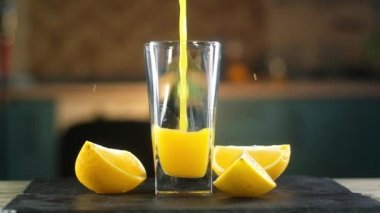 Taze portakal suyu mutfak arka plan karşı siyah tepsi üzerinde duran açık cam kadeh içine dökülür. Sonraki meyve dilimleri etrafında sıçrama bir sürü olduğunu. Stüdyo aydınlatmaile panoramik çekim.