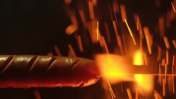薄い金属串に揚げたジューシーなバラ色のソーセージのパノラマクローズアップショット 火の熱い炎の上にぶら下がっている 周りに火花を燃やす — ストック動画
