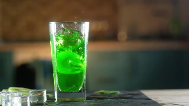 圆形的成熟奇异果片落入玻璃湿玻璃中的绿色起泡水中 杯子放在黑色托盘上 有冰块和薄荷叶 周围有很多喷雾 带工作室照明的全景拍摄 — 图库视频影像