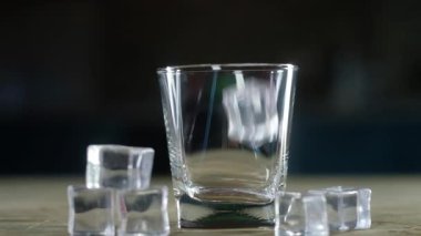 Buz küpleri temiz, boş bir malt bardağa düşer. Dipten zıplayıp dön. Cam siyah bir standın üzerinde. Buz kristallerinin yanına uzan. Kapatın. Uzmanlar için alkollü bir içecek..