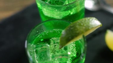 Kenarlarında ıhlamur parçaları olan bardaklarda şenlikli yeşil kokteyller. Soğuk buz küpleri karbonatlı içeceğin içinde yüzer. Noel tatili. Panorama saldırısı. Yukarıdan görüntüle.