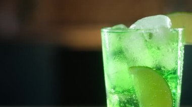 Islak bardakta temiz su damlalarıyla yeşil kokteyl ve büyük buz küpleriyle. Camın kenarına bir dilim taze kireç konmuş. Yılbaşı içkilerinin panoramik çekimi