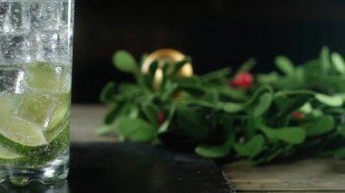 Köpüklü limon dilimleri ve soğuk buz küpleriyle dolu berrak bardaklar Noel süslemelerinin arka planında yer alıyor. Şenlikli bir kokteylin panoramik çekimi
