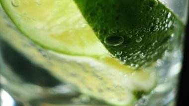 Bir bardak köpüklü suda sulu kireç parçaları yüzüyor. Neşelendirici bir toniğin makro fotoğrafçılığı