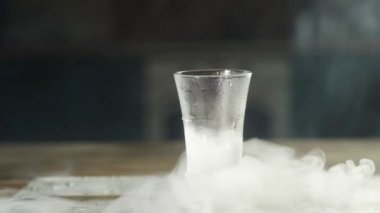soğuk buhar yavaş yavaş votka bir buz bardağı olduğu ahşap bir masa üzerinde dalgalar sürünür. camdan standa büyük su damlaları.