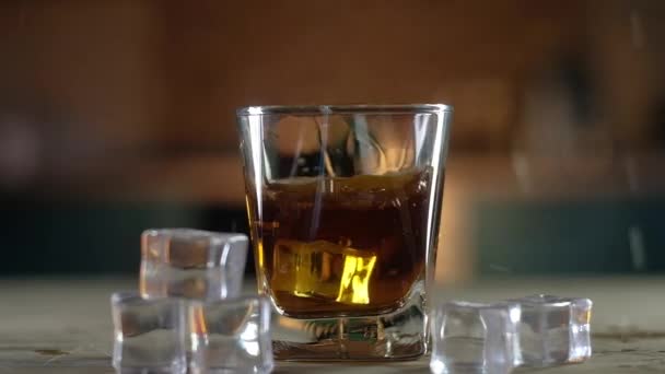 Ice cubes fall into a clear glass of strong single malt whiskey making a big splash. The glass is on a black stand. Lay next to the ice crystals. Festive alcoholic drink for connoisseurs. — Stock Footage Ice Cubes Fall Clear Glass Strong Single Malt Whiskey Making Stock Footage
