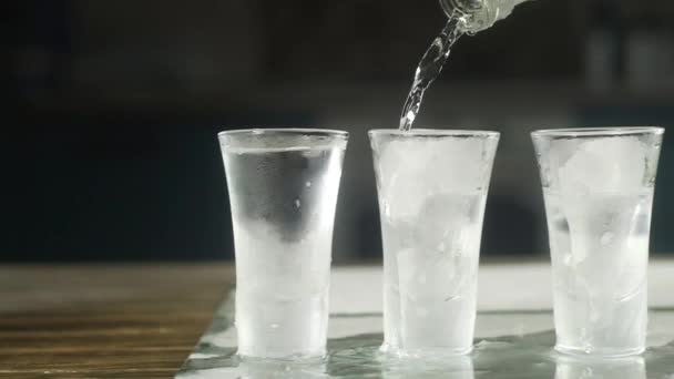 Der Barkeeper Gießt Wodka Aus Einer Flasche Mehrere Eisige Gläser — Stockvideo