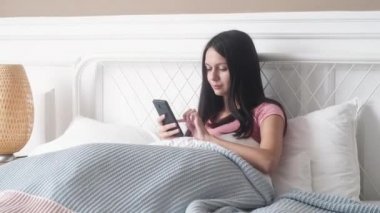 Genç ve güzel bir kız telefonuyla yatakta oturuyor ve bir mesaj yazıyor. Aletini komodinin üzerine koyar ve kendini battaniyeye sarar. Kadın uyumak istiyor.