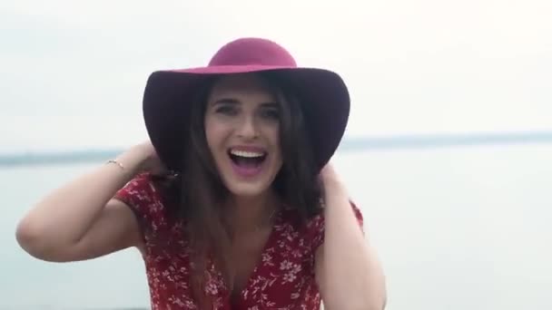 海的背景上穿着红色长发的纤细少女的画像 女人顶着粉红的帽子迎风 笑着享受自由 远离文明 一帆风顺 — 图库视频影像