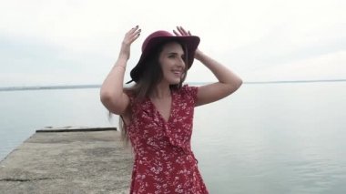 Kırmızı elbiseli, siyah şapkalı, uzun saçlı genç ve sevimli bir kız rıhtımda durmuş kameraya gülüyor ve flört ediyor. Neşeli bir kadın. Duygusal olarak deniz kenarında dinleniyor. Sessizliğin ve yalnızlığın tadını çıkarıyor.