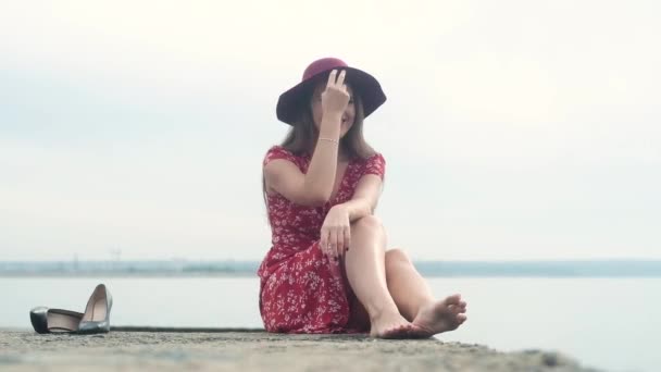 Cheerful Attractive Girl Red Dress Pink Hat Sits Stone Sea — Stock Video