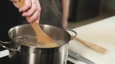 Kapat. Evdeki mutfakta makarna pişirmek. İtalyan yemek tarifi. Aşçı ahşap bir spatulayla erişteyi kaynamış bir tencerede kaynatır. Bir adam akşam yemeği için makarna yapar..