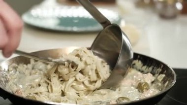 Profesyonel şef mutfakta çalışıyor. Şef, çatallı beyaz krema soslu spagetti büküyor. Evde makarna pişirmek. Tabağın süslemesi. Evde mutfakta yemek pişirmek..