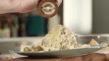 Soslu İtalyan makarnası pişirmek. Pişirmek, karabiber kokulu biber ve biber karıştırmak. Yakın plan. Adam evdeki mutfakta yemek pişiriyor ve bir tabağa baharat ve baharat döküyor.