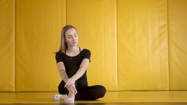 身穿黑色衣服的身材苗条的小女孩正坐在体育馆里 房间里的瑜伽课 放松和冷静 一个白人女人在瑜伽之后休息 现代世界的健康生活方式 — 图库视频影像