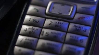 Eski, çizilmiş, tozlu cep telefonları mavi neon ışıkta masanın üzerinde duruyor. Klavyedeki eski cep telefonlarının makro atışları. Ofiste analog iletişim. Modern kablosuz teknoloji