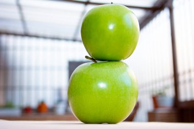 Üst üste iki yeşil elma arka planda bazı bitkiler ile yakın