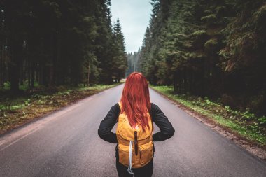 Kızıl saçlı kız huzurlu ormanda tek başına. Sırt çantası yolda olan bir kız. Viem arkadan ve boş yoldan.