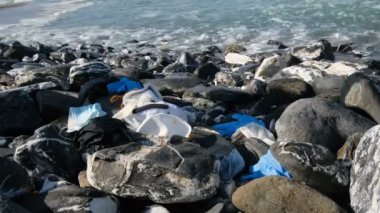 Adam deniz kıyısında tıbbi atık topluyor, maskeler, plastik eldiven, koronavirüs kirliliği.