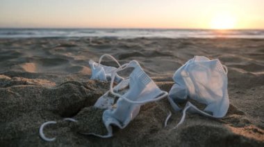 Tıbbi atıkların gün batımı, deniz sahilinde yüz maskesi çöpleri, yürüyen insanlar, covid19 virüs salgını kirliliği. 