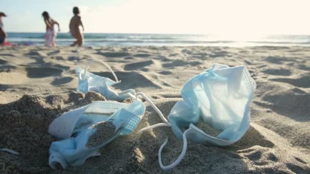 Медицинские отходы, маска для лица выброшенный мусор, дети играют на морском пляже, Covid19 вирус пандемии загрязнения — стоковое видео