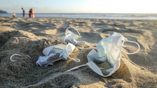 Timelapse di scartati rifiuti maschera medica sulla costa del mare con persone a piedi sfondo, covid19 virus pandemico inquinamento — Video Stock