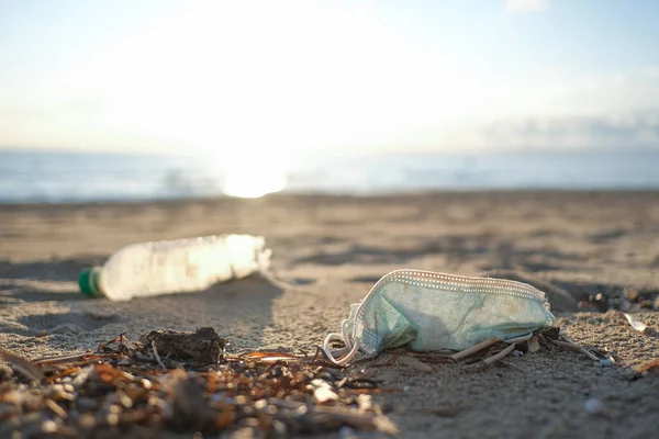 Medical face mask and plastic bottle discarded on dirty sea coast,covid19 pandemic disease pollution effects