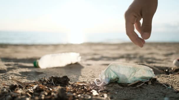 Доброволец собирает использованную маску для лица и пластиковую бутылку на грязной морской экосистеме, загрязненную окружающей средой — стоковое видео