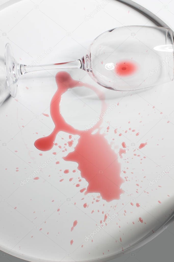 Overturted empty wine glass lies on spilled red wine