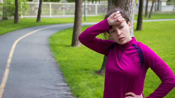 Tired young athletic woman runner wipes sweat from forehead,taking rest after jogging workout hard with focus and determination to take on weight loss cardio goal achievement challenge. — Stock Photo, Image