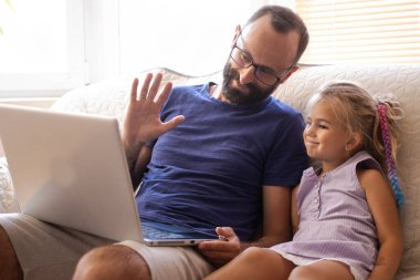 Küçük kızı olan genç sakallı mutlu bir baba dizüstü bilgisayarla video görüşmesi yapıyor, selam veriyor, anneyle ya da dedemle konuşuyor kablosuz internet bağlantısı kuruyor, evdeki kanepede oturuyor.. 