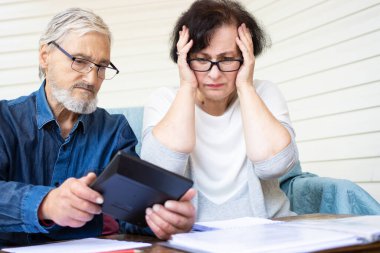 Scared and worried senior couple looking at calculator, counting bank loan payment, calculating bills managing domestic finances. Worried about bankruptcy or money problem. Little savings concept clipart