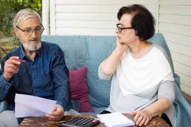 Ciddi endişeli yaşlı çift ödenmemiş banka borçları, ödenecek faturaların hesaplanması ya da iç maliyenin kontrol edilmesi, ev teraslarındaki kanepede oturması gibi evrakları okuyor. İflas para sorunları kavramı.