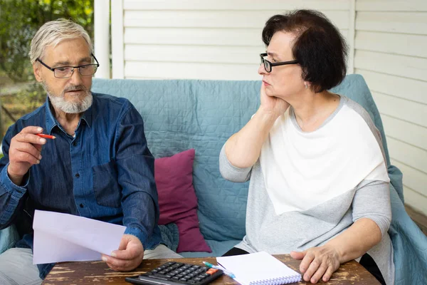 Ciddi endişeli yaşlı çift ödenmemiş banka borçları, ödenecek faturaların hesaplanması ya da iç maliyenin kontrol edilmesi, ev teraslarındaki kanepede oturması gibi evrakları okuyor. İflas para sorunları kavramı.