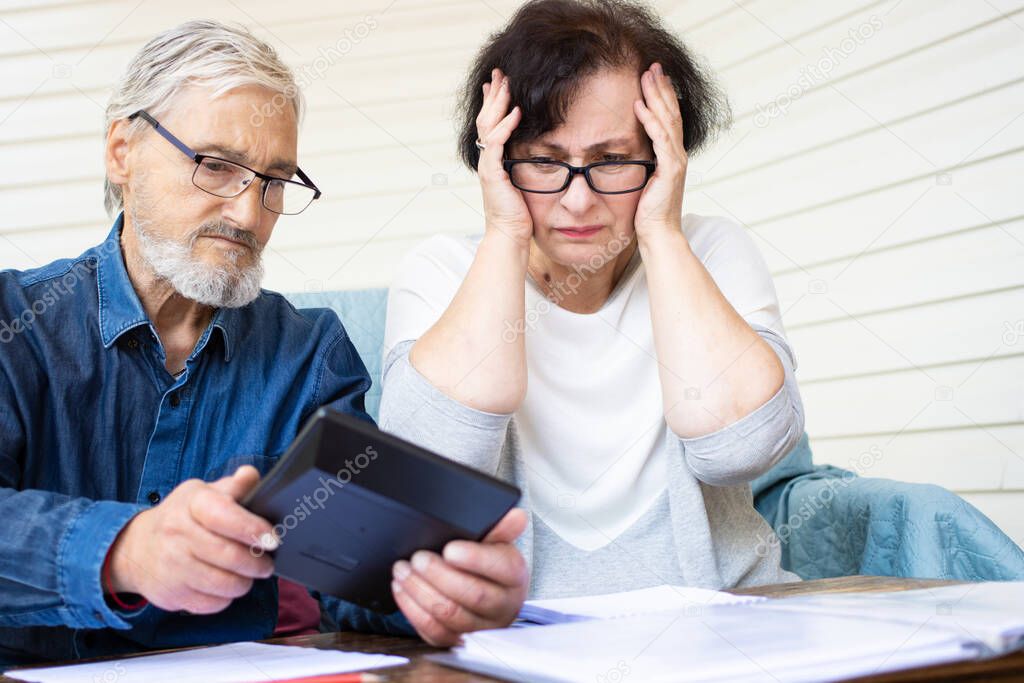 Scared and worried senior couple looking at calculator, counting bank loan payment, calculating bills managing domestic finances. Worried about bankruptcy or money problem. Little savings concept
