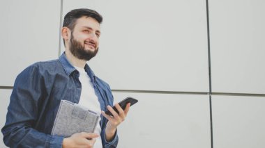 30 'lu yaşlarda esmer sakallı bir adamın portresi. Kot giyer, elinde cep telefonu taşır. Kablosuz internet bağlantısı kullanır.. 