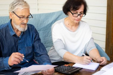 Odaklanmış ciddi üst düzey çiftler kağıt belgeleri okuyor ve finansman için faturaları hesaplıyor, aile içi harcamaları yönetiyor, bütçeyi planlıyor, terasta kanepede oturuyor..