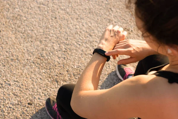 Athlete woman touching fitness tracker checking pulse or sport information, adjusting setting smart watch before running or morning workout session, sitting outdoors in summer sunshine day.Copy space