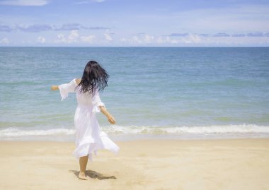 Beyaz elbise giyen, mutlu, eğlenen, tatilde rüzgarlı ve güneşli plajda rahatlayan genç bir kadının bulanık hareketi..