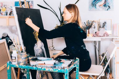 Atölyede siyah sehpada resim yapan kadın.