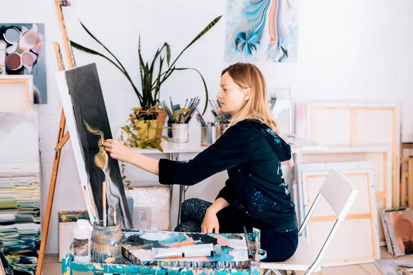 Atölyede siyah sehpada resim yapan kadın.