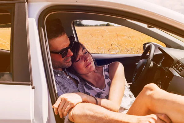 pleased couple enjoy the silence of the countryside embracing inside a parked car. relax, joy, freedom, love, togetherness and slow down concept.