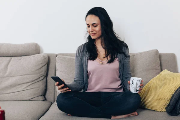 Kvinne Som Sitter Sofaen Holder Mobiltelefon – stockfoto