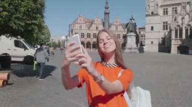 Güzel, gülümseyen genç bir kadın cep telefonu kullanıyor. Kadın turist selfie çekiyor ve şehir merkezinde video kaydediyor.