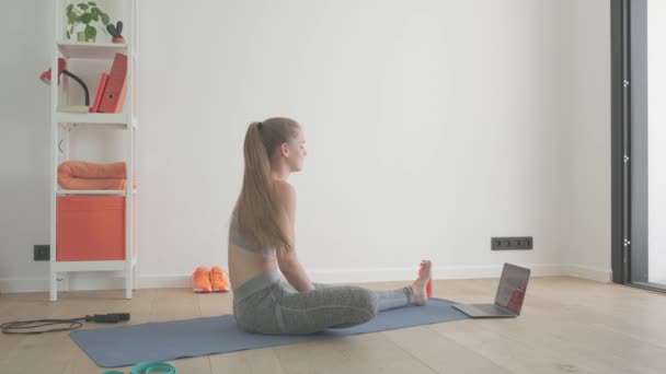 在家里穿着运动服躺在瑜伽垫上的健康女性正在使用笔记本电脑进行锻炼 运动娱乐技术概念 — 图库视频影像