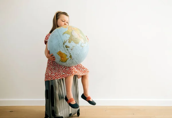 World Tourism Day Concept. Girl sitting on a trolley holding and looking to the earth globe and dreaming to travel the planet