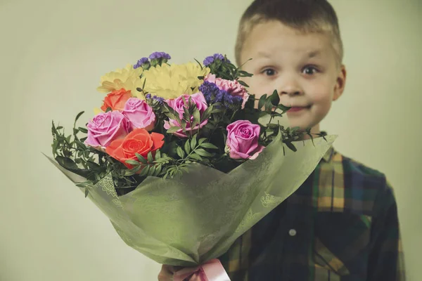 緑の背景に花の美しい花束を持つ面白い少年 — ストック写真